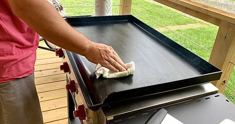 man seasoning gas griddle with paper towel