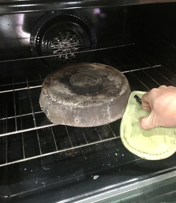 man's hand putting cast iron skillet inside oven upside down