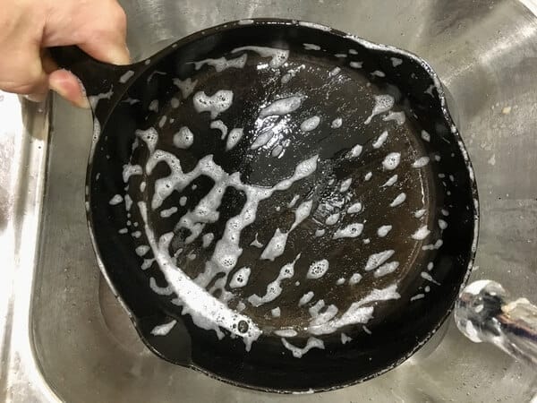cast iron skillet being washed with soap