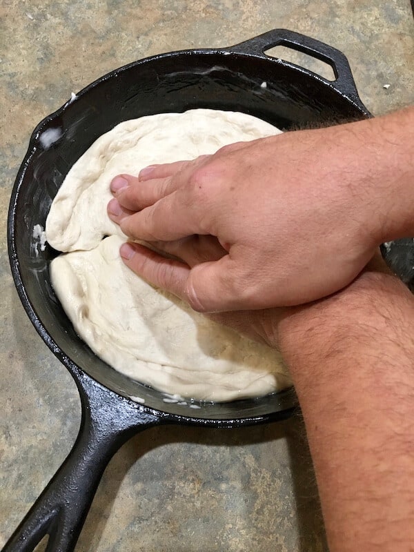 hands kneading pizza dough inside a cast iron skillet