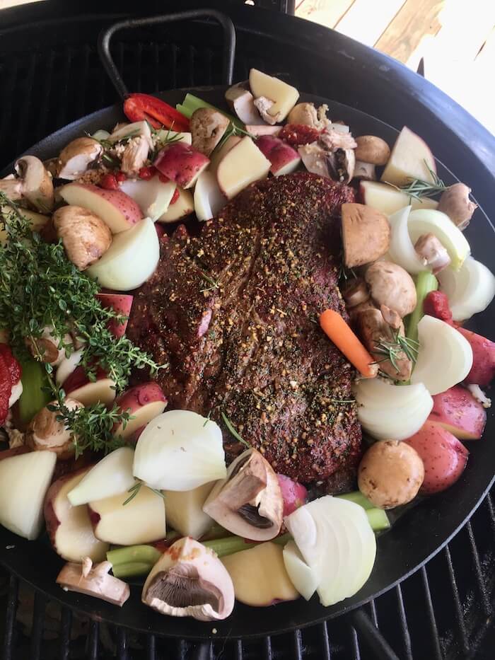 pot roast and vegetables in a pan on a charcoal grill