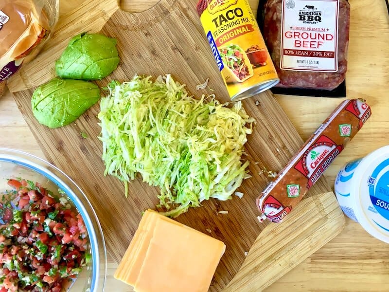 ground beef, chorizo, taco seasoning, lettuce, avocado, pico de gallo, and cheese on a cutting board