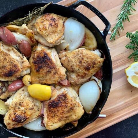 chicken thighs potatoes garlic onions and lemon in a cast iron skillet