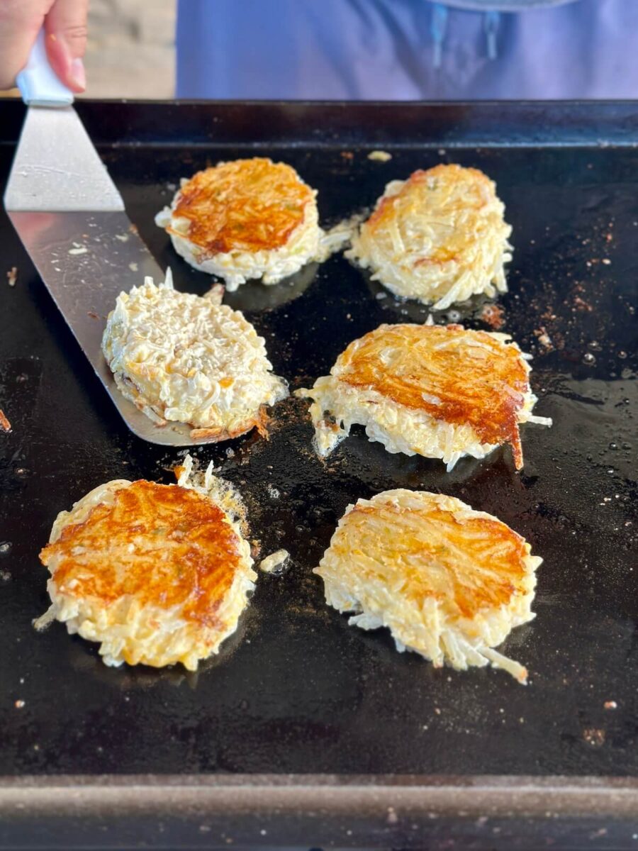 using a spatula to flip a hash brown casserole cake on a griddle