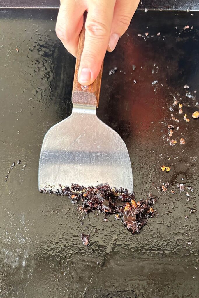 cleaning a Blackstone griddle surface with a scraper