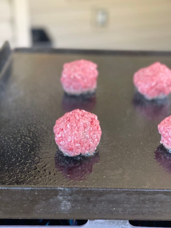 ground beef rolled into balls on a flat top grill