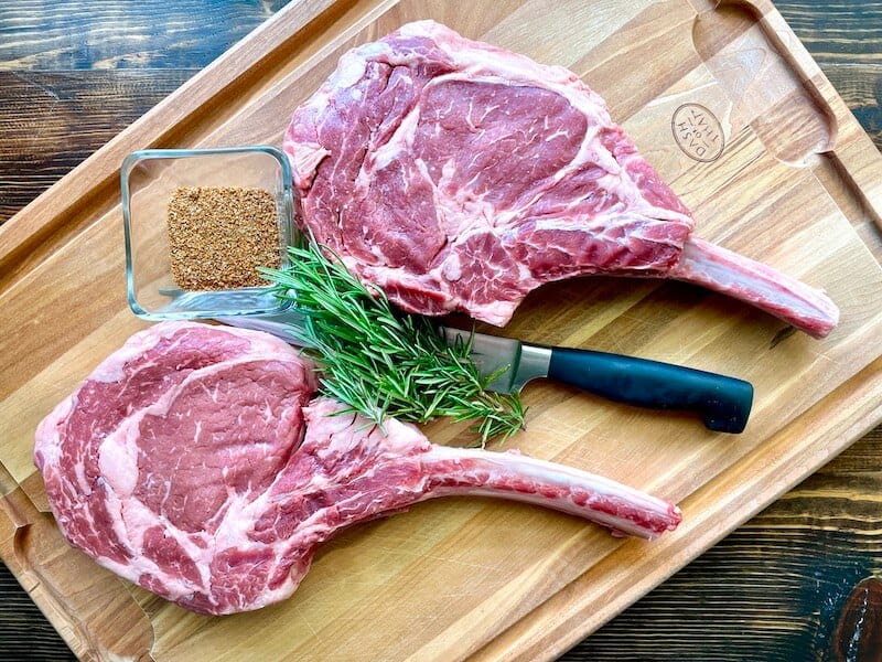 2 uncooked thick cut steaks on a cutting board