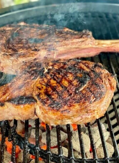 2 tomahawk ribeyes searing on a charcoal grill
