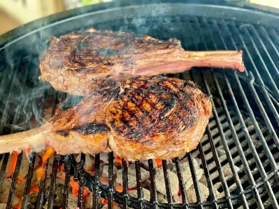 2 tomahawk ribeyes searing on a charcoal grill