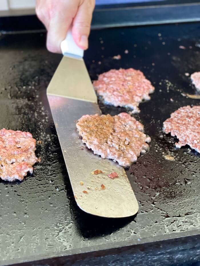 using a griddle spatula to flip smash burgers