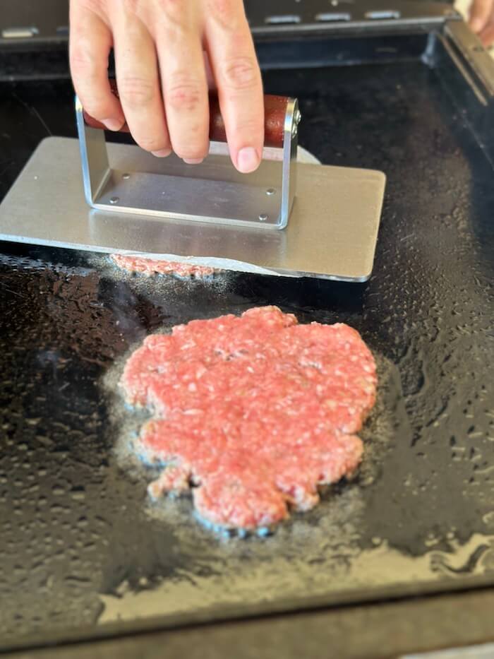 using a burger press to make smash burgers on the griddle