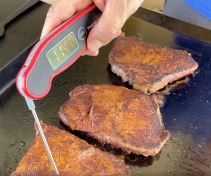 using an instant read thermometer in a steak on the flat top grill