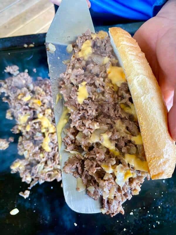 using a spatula to put cheesesteak on a roll