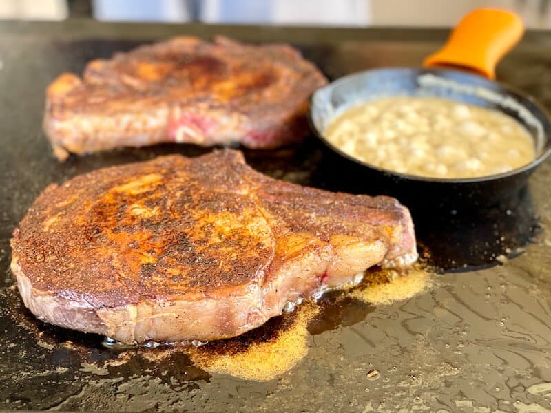 ribeye steaks and cream sauce cooking on a flat top grill