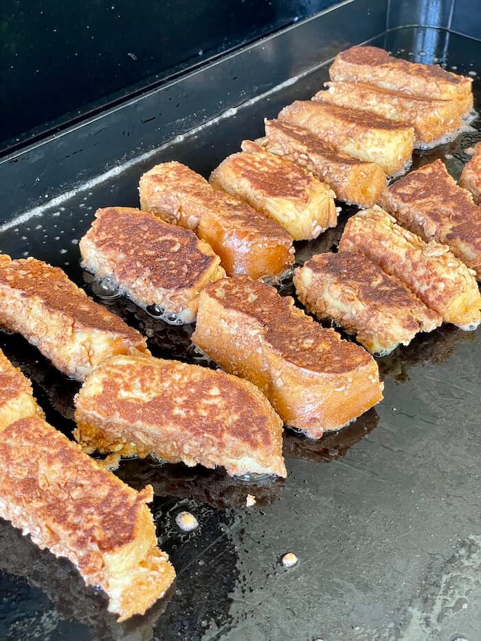 french toast sticks coated in cinnamon toast crunch cereal cooking on a griddle