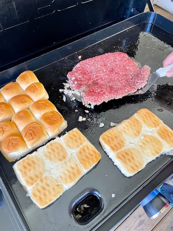 slider buns and ground beef cooking on a griddle