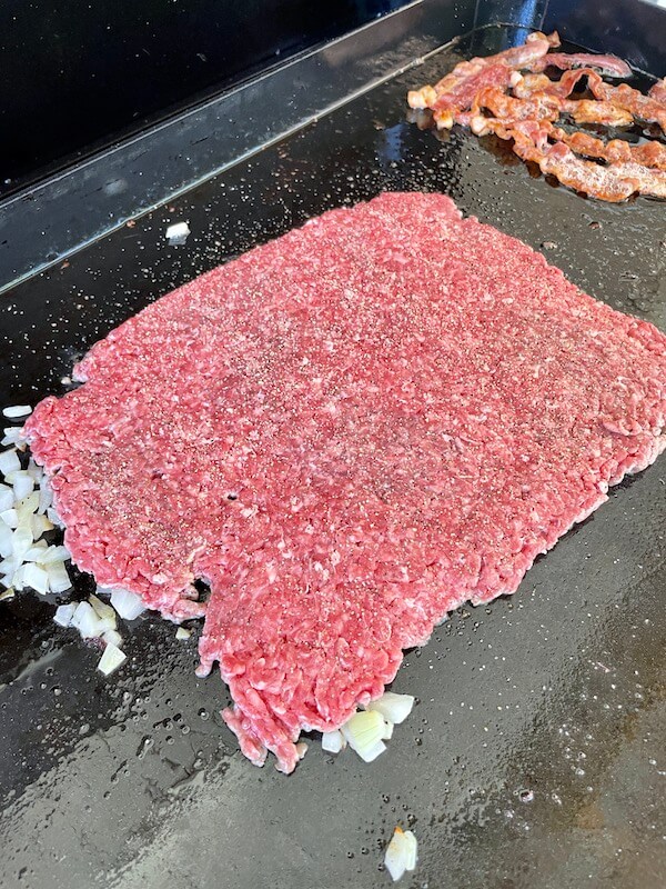 ground beef cooking in onions on a flat top grill