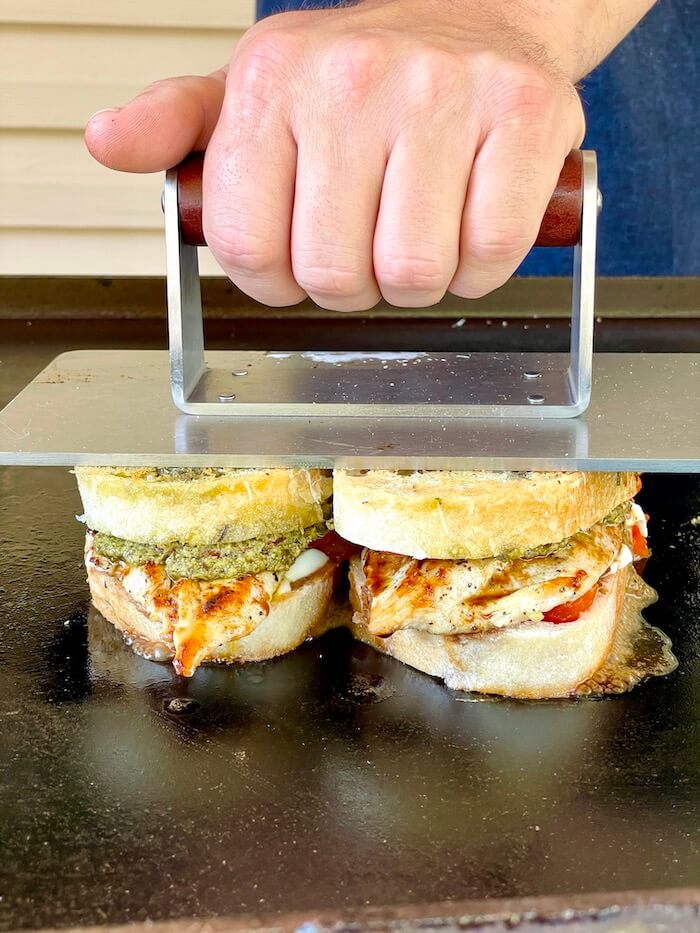 using a press to make a chicken caprese panini sandwich on a flat top grill