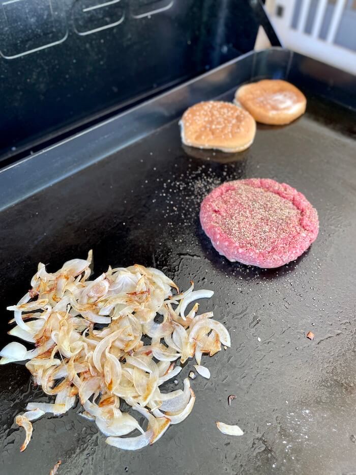 onions and Juicy Lucy burger cooking on a griddle