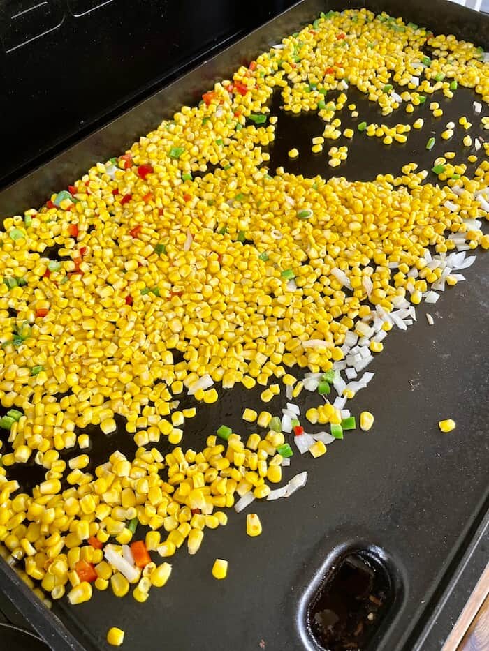 corn, peppers, and onions cooking on a griddle