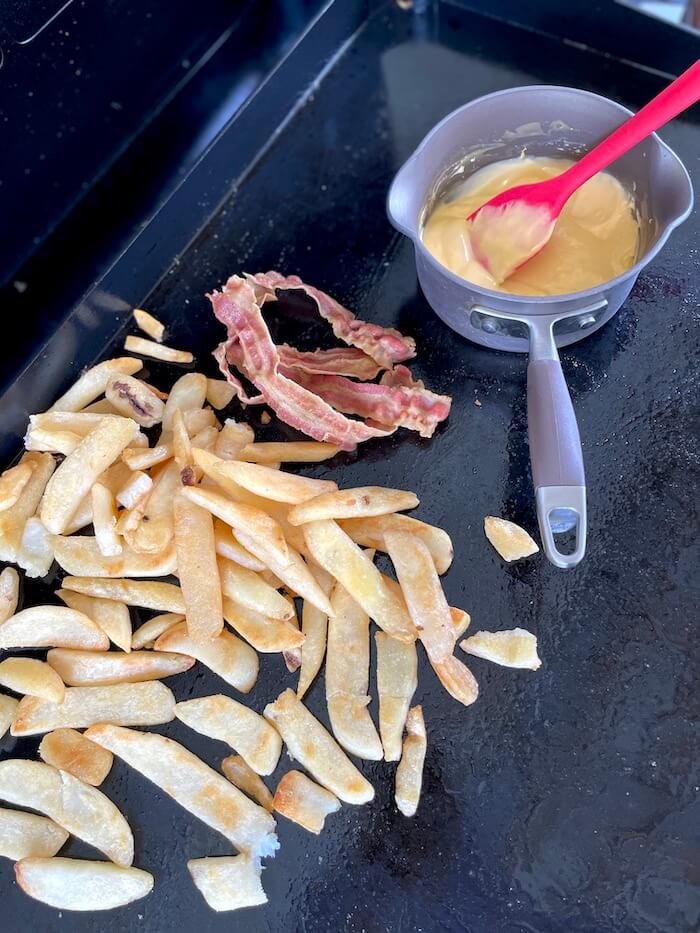 french fries, bacon, and cheese sauce cooking on a griddle