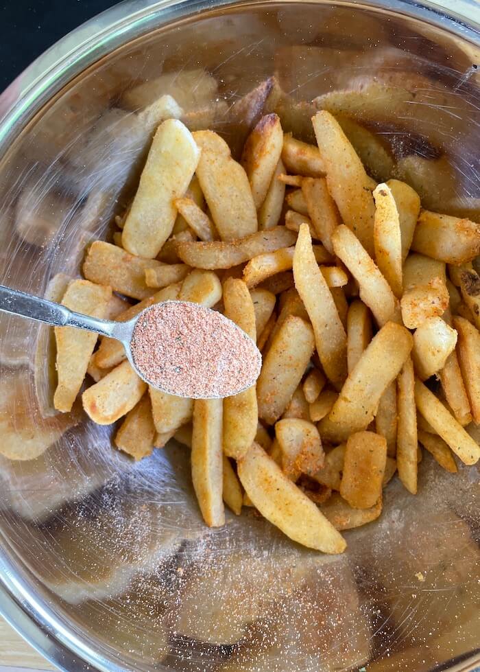 adding french fry seasoning to cooked french fries