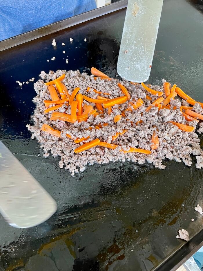ground sausage, ground beef, and carrots cooking on a Blackstone griddle