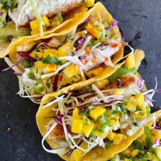 fish tacos with halibut, shredded cabbage, and mango pico de gallo on corn tortillas