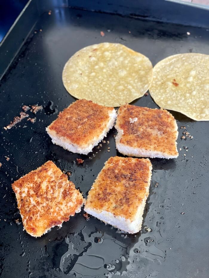 fish filets cooking on a griddle with corn tortillas