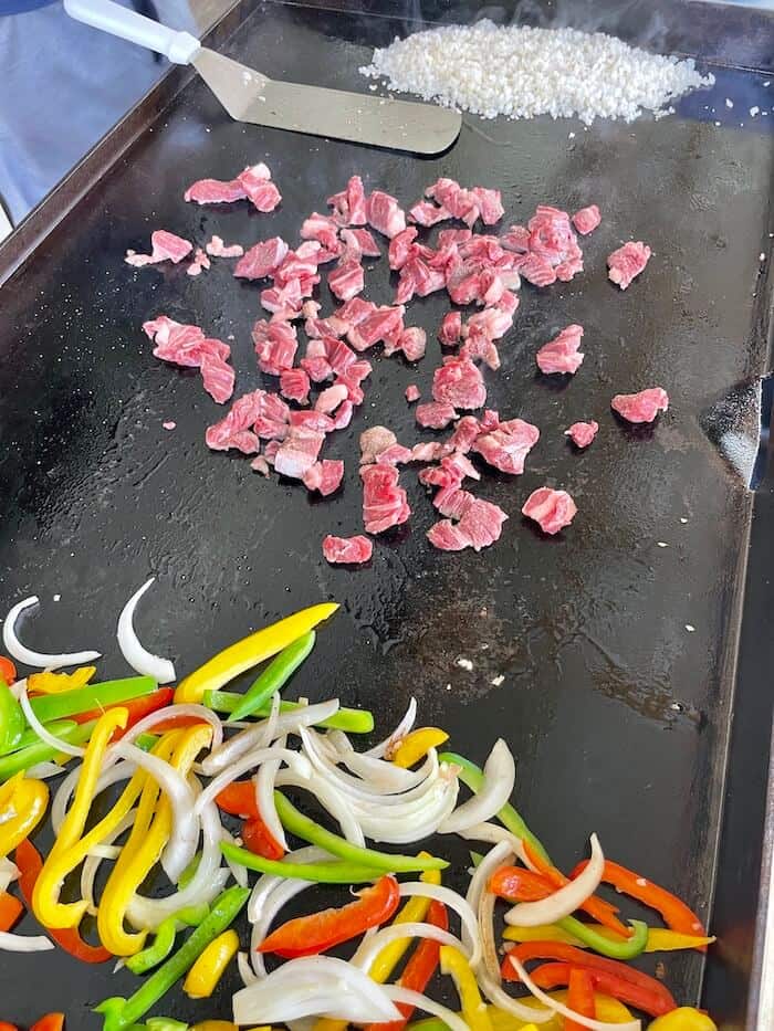 bell peppers, onions, steak, and rice cooking on a Blackstone griddle