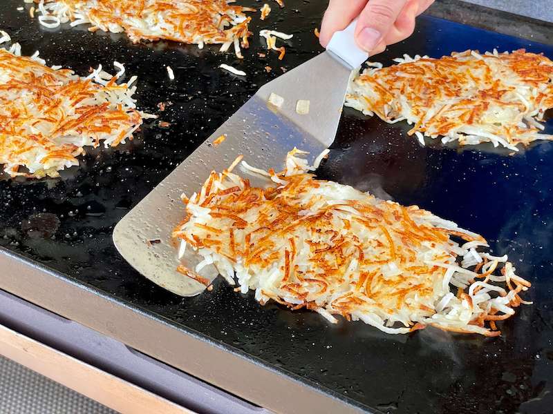 using a spatula to flip hash browns on griddle
