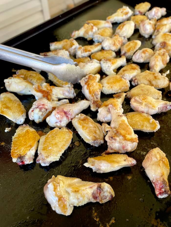 flipping chicken wings with tongs on a griddle