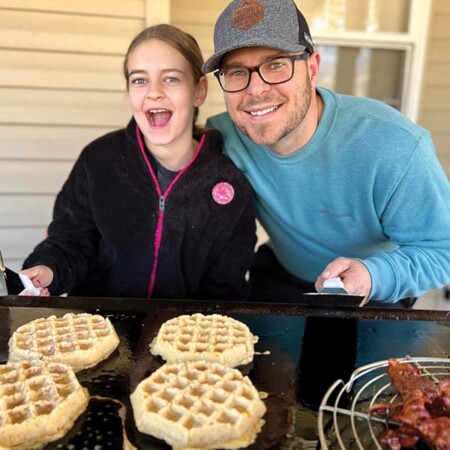 Neal and daughter smiling cooking waffles.