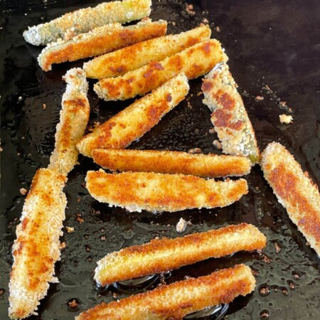fried pickle spears cooking on a griddle