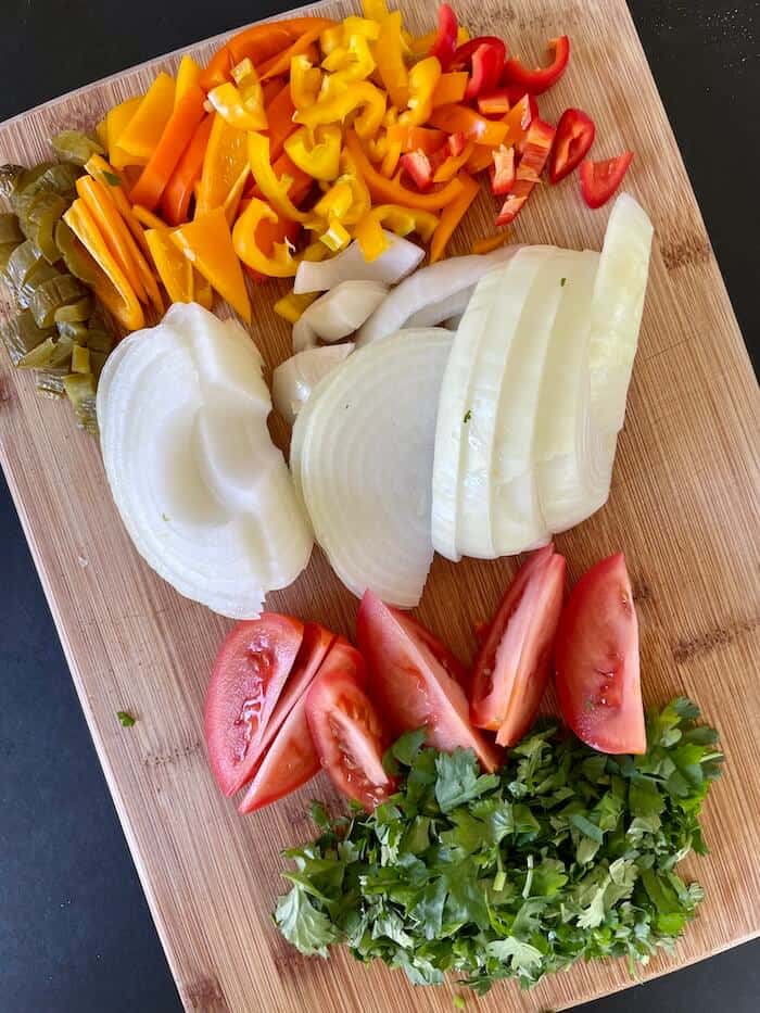 sliced bell peppers, onions, tomatoes, and cilantro on a cutting board