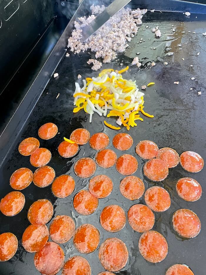 sliced pepperoni, sausage, and vegetables cooking on a griddle for pizza quesadillas