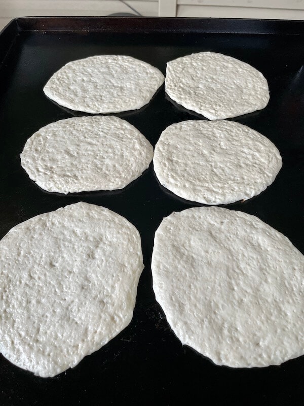 Pillsbury biscuits that have been rolled out thin cooking on a Blackstone griddle