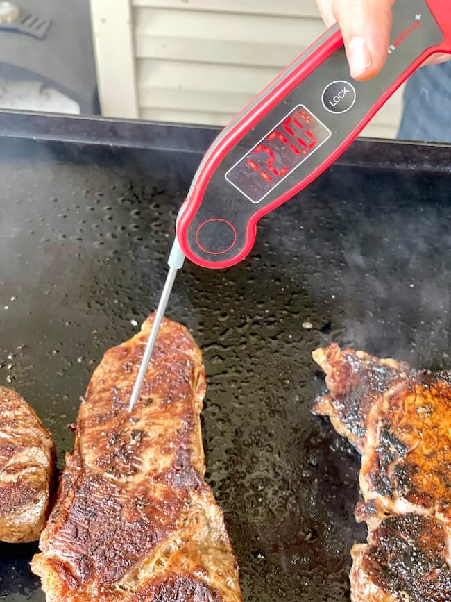 using an instant read thermometer to check the internal temp of a steak on the griddle