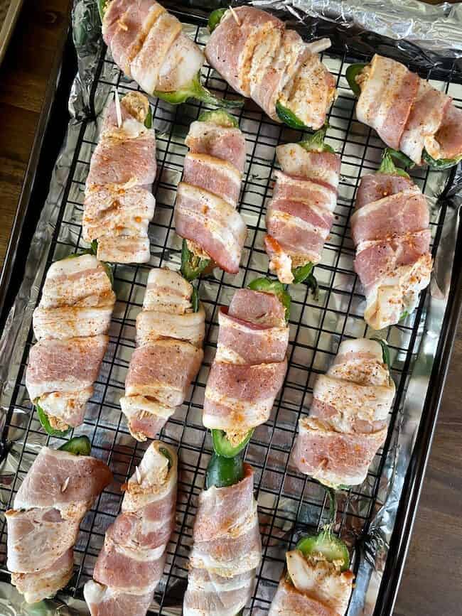 stuffed bacon wrapped jalapeno poppers on a sheet tray and cooling rack