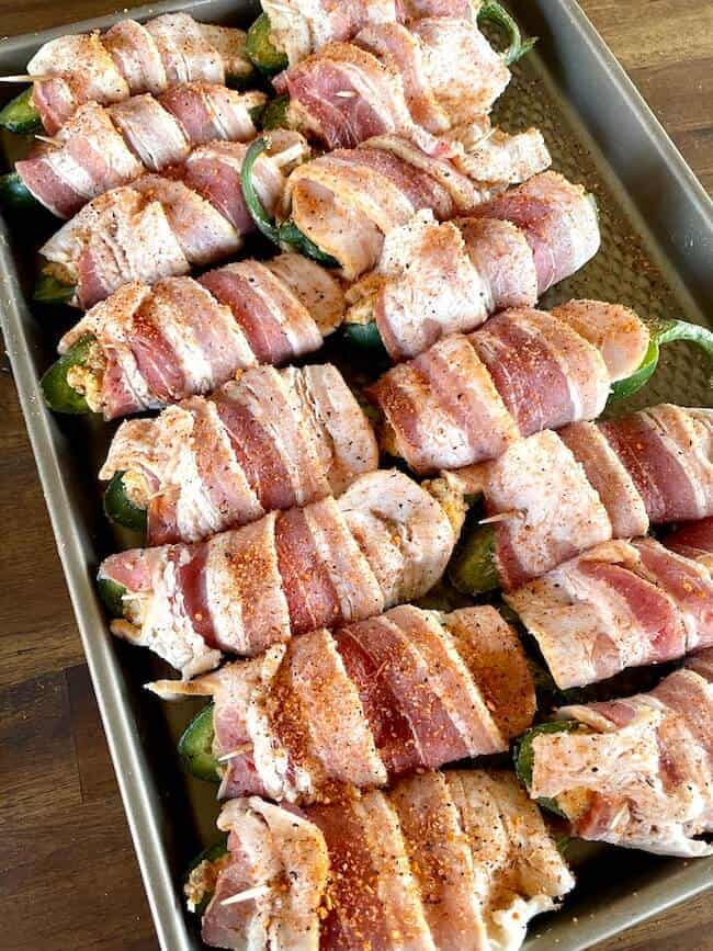 bacon wrapped jalapeno poppers with cream cheese filling on a baking sheet
