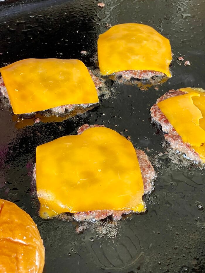 cheese burgers cooking on a griddle