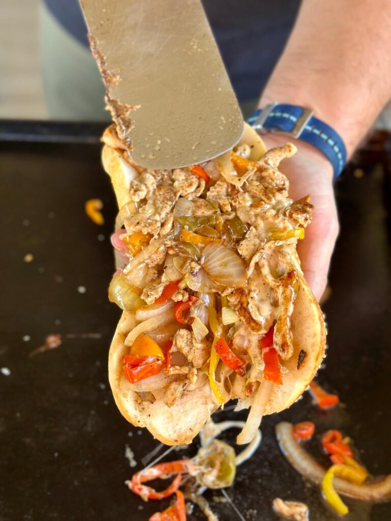 adding chicken cheesesteak mixture to a hoagie roll
