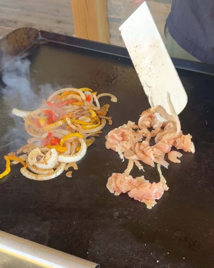 cooking chicken strips and sliced vegetables on a griddle