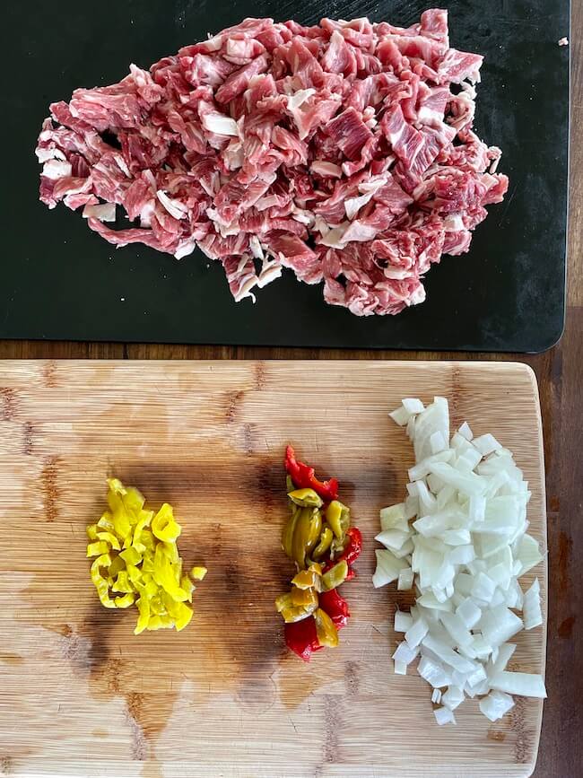 sliced ribeye, diced onions, and diced banana peppers and sweet cherry peppers on a cutting board