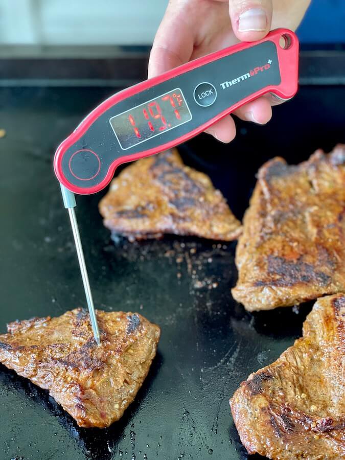 using an instant read thermometer to test the temperature of a skirt steak on the griddle