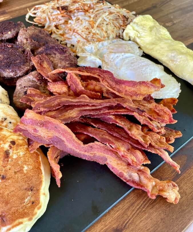 bacon on a cutting board with other griddle breakfast foods