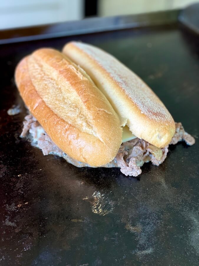 hoagie roll turned upside down steaming over a pile of cheesesteak on a Blackstone griddle