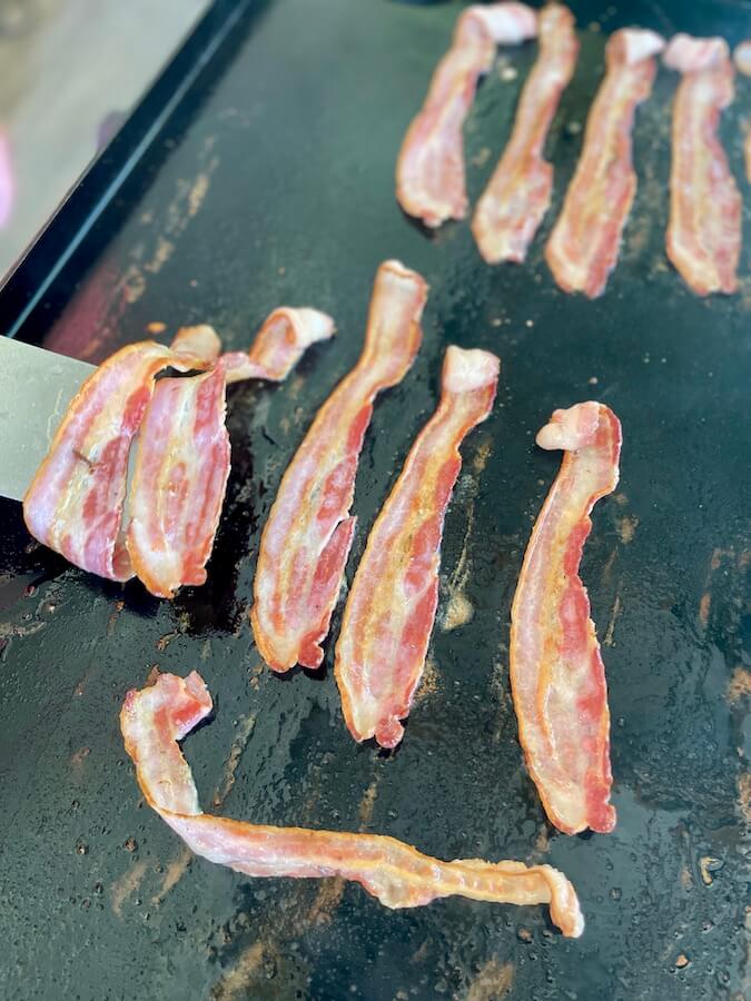 using a spatula to flip bacon on the griddle