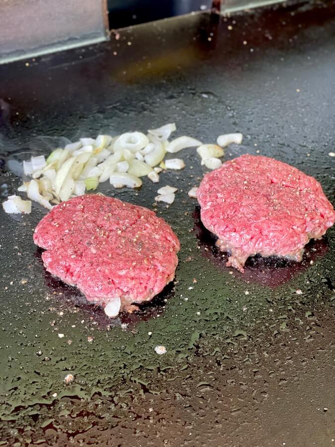 ground beef patties and diced onions cooking on a griddle