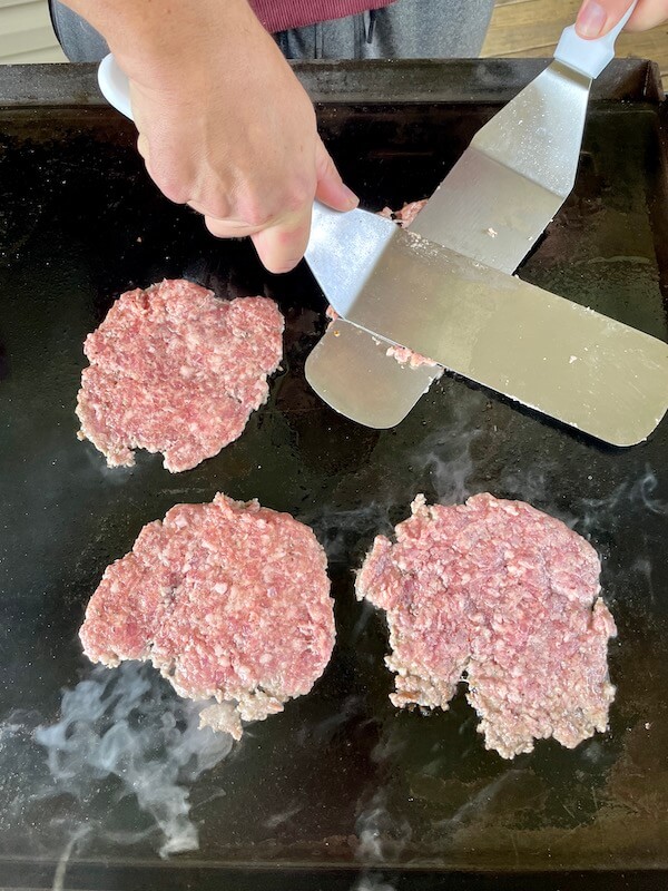 using two spatulas to press down on burgers on the Blackstone